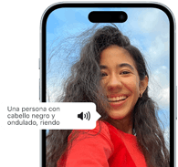 Un iPhone&nbsp;15 muestra cómo la funcionalidad VoiceOver lee la descripción de una imagen: una persona con pelo negro ondulado sonriendo